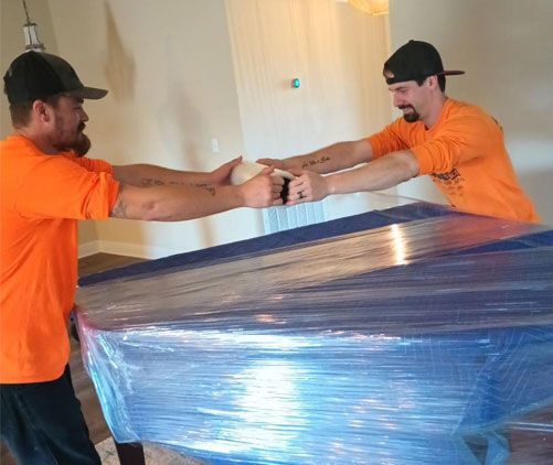 Two men are wrapping a piano in plastic wrap.