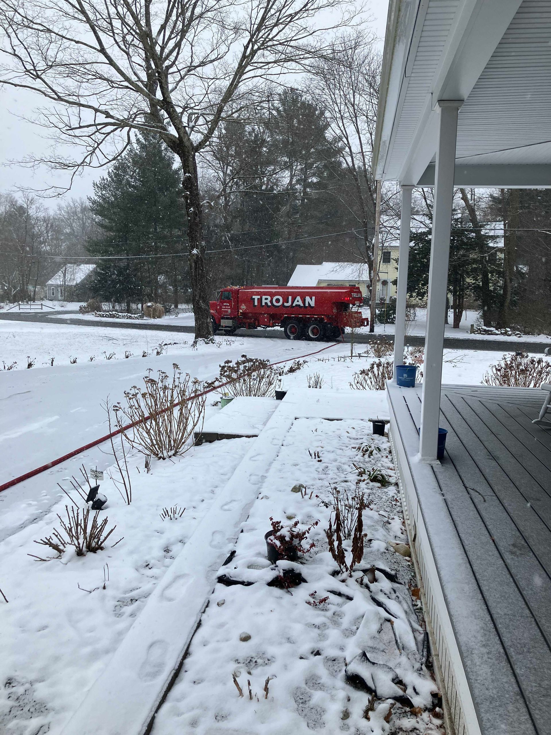 Red emergency truck on a snowy suburban street beside a white porch.