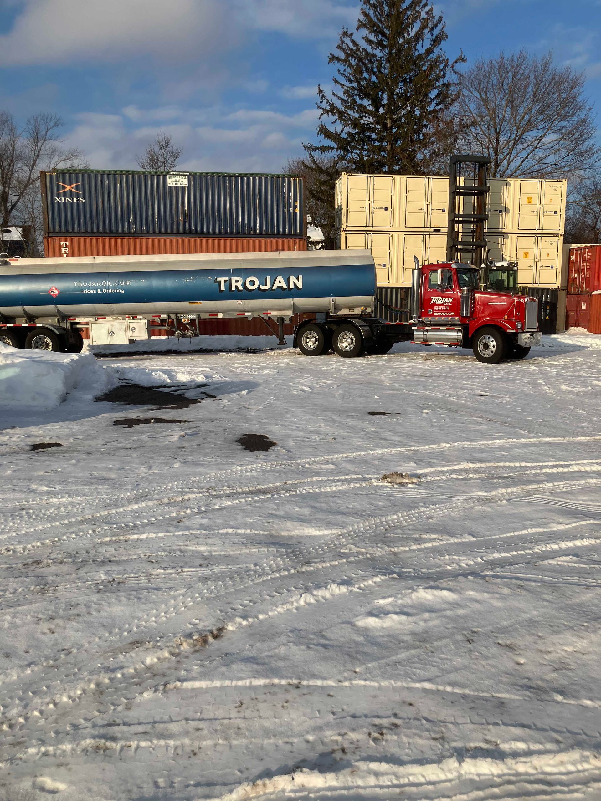 Red truck with tanker and stacked crates in a snowy industrial yard on a clear day
