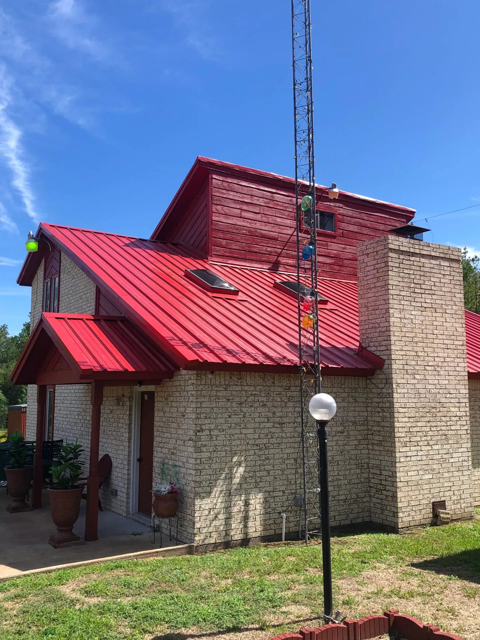 A brick house with a red roof and a wind chime in front of it.