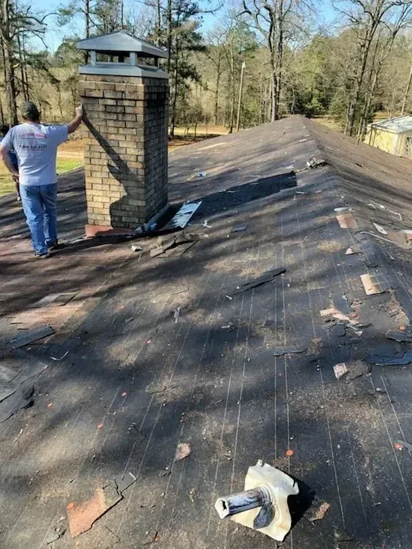 A man is standing on top of a roof next to a chimney.