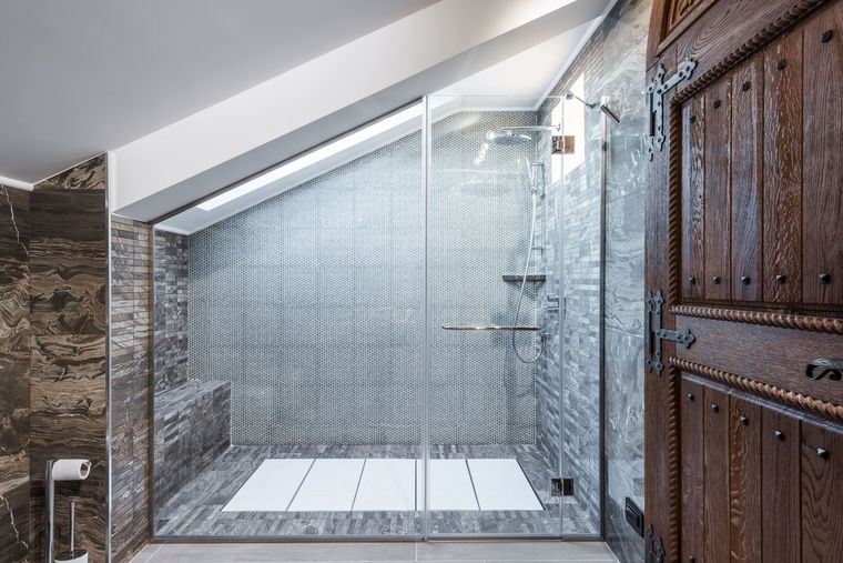 Modern glass-tiled shower under a slanted skylight, with white floor tiles and wooden doors on the right