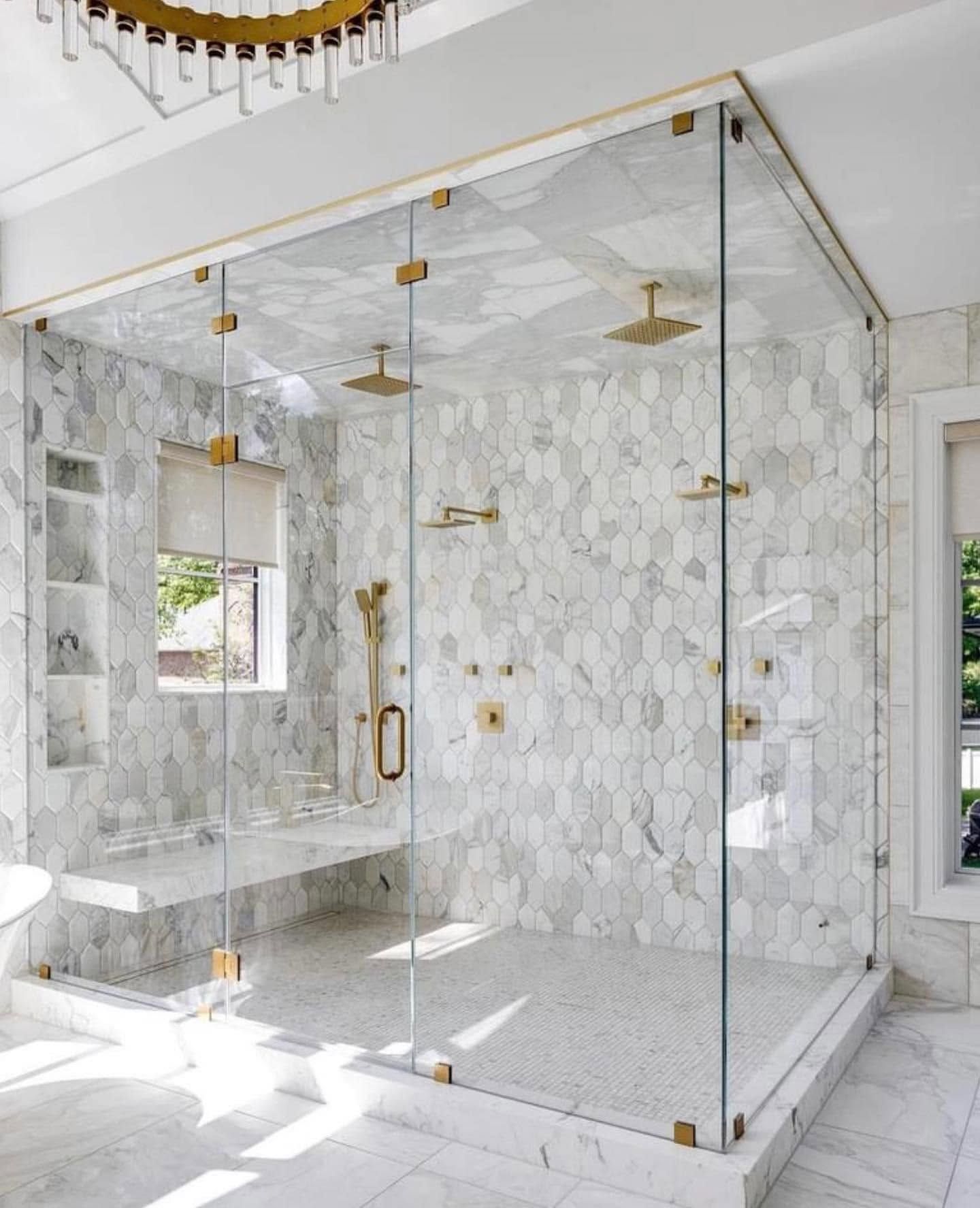 Luxurious marble-tiled walk-in shower with glass enclosure and gold fixtures, brightly lit with a window.