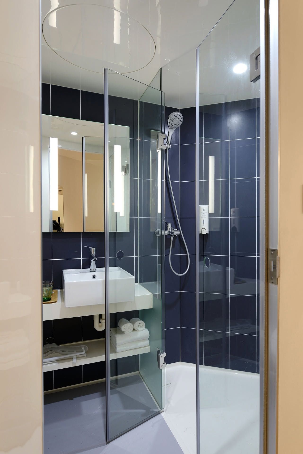 Modern bathroom with glass shower, white sink, dark tile, and large mirror.