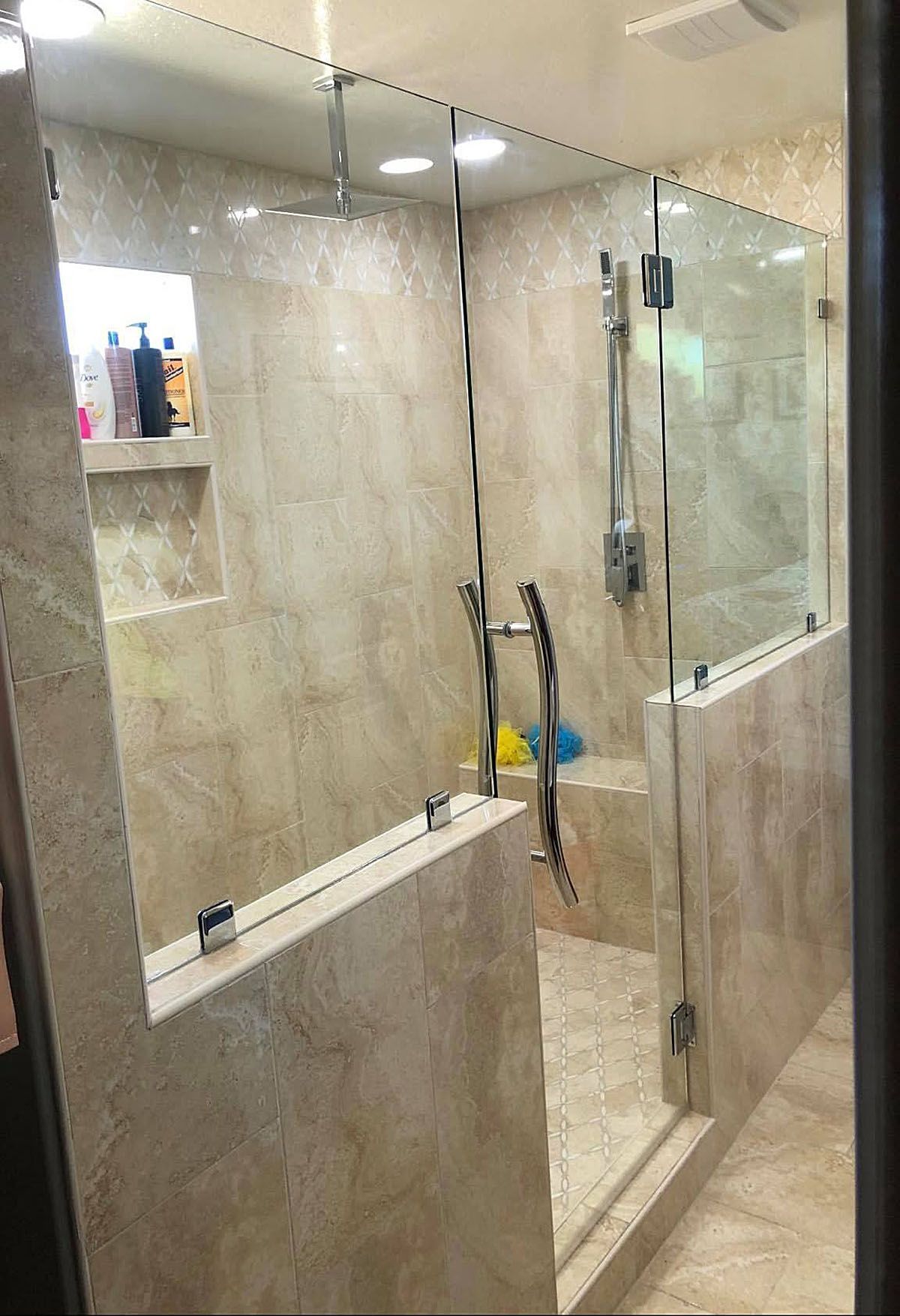 Walk-in tiled shower with glass doors, chrome fixtures, and cleaning tools inside.