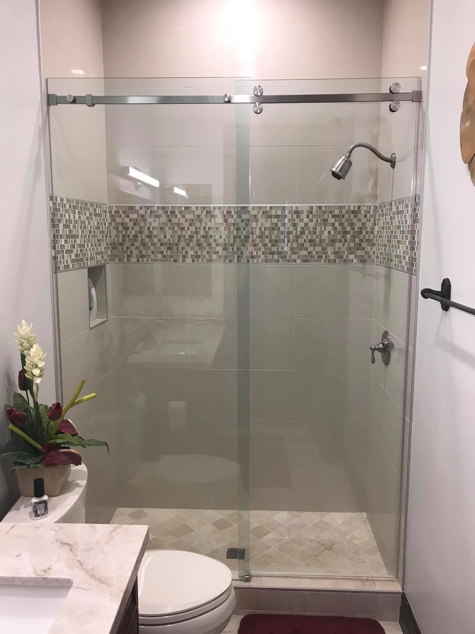 Small bathroom with glass-enclosed shower, mosaic tile band, white toilet, and sink counter with flowers.
