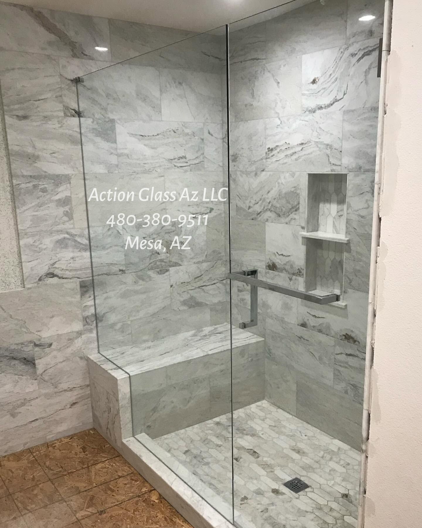 Glass walk-in shower with gray tile, bench, and built-in shelves in a bathroom showroom.