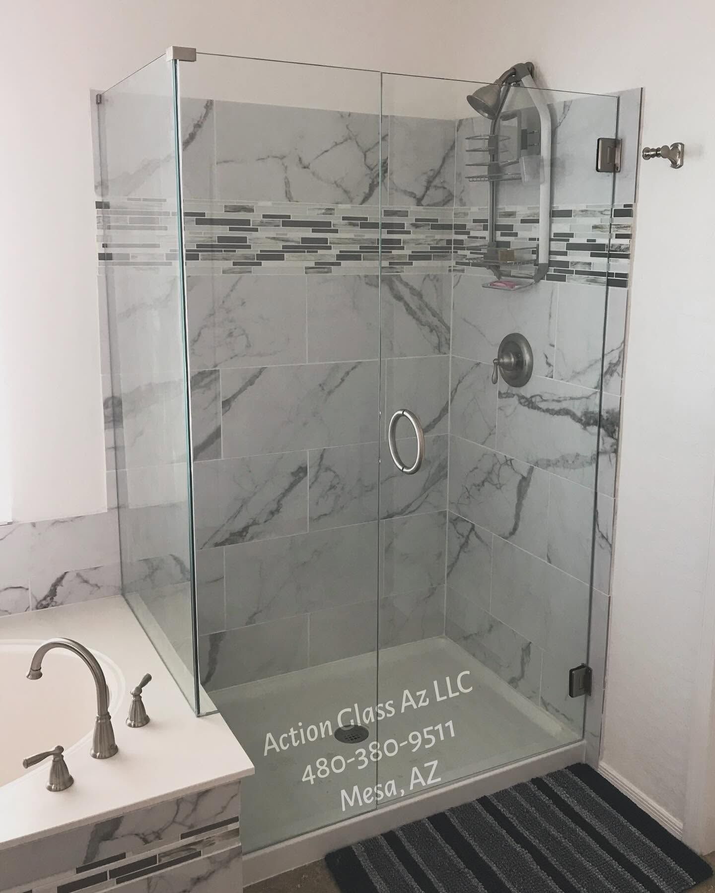 Modern glass shower enclosure with marble-look tile and chrome fixtures in a bathroom showroom.