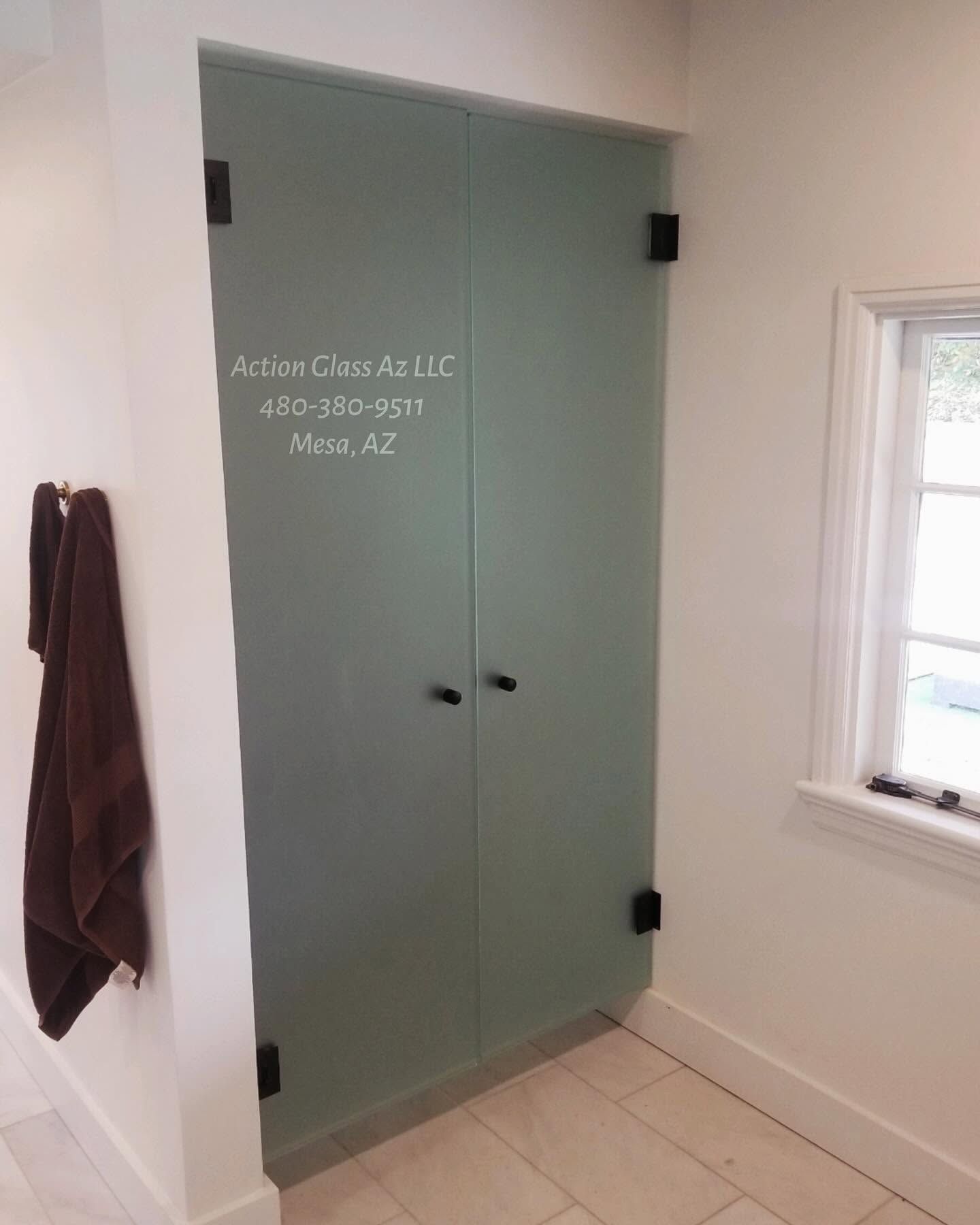 Green bathroom cabinet beside a towel and window on beige tile floor.