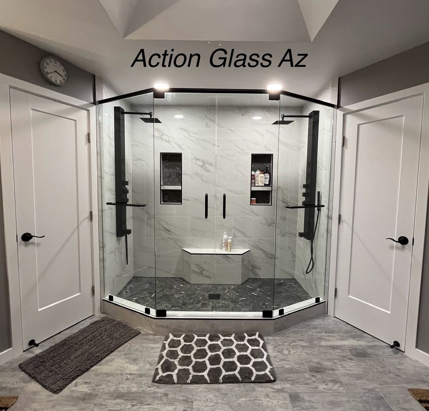Modern glass shower enclosure in a bathroom showroom with white doors and gray floor mats.