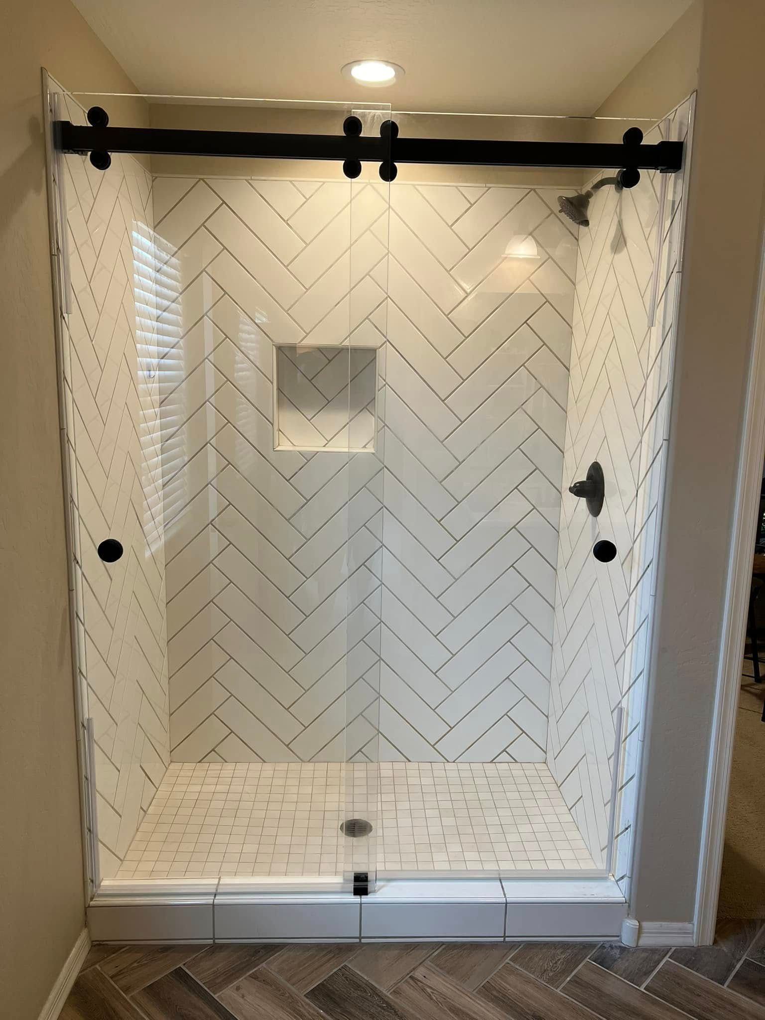 White tiled bathroom shower with sliding glass doors and black hardware, seen head-on.