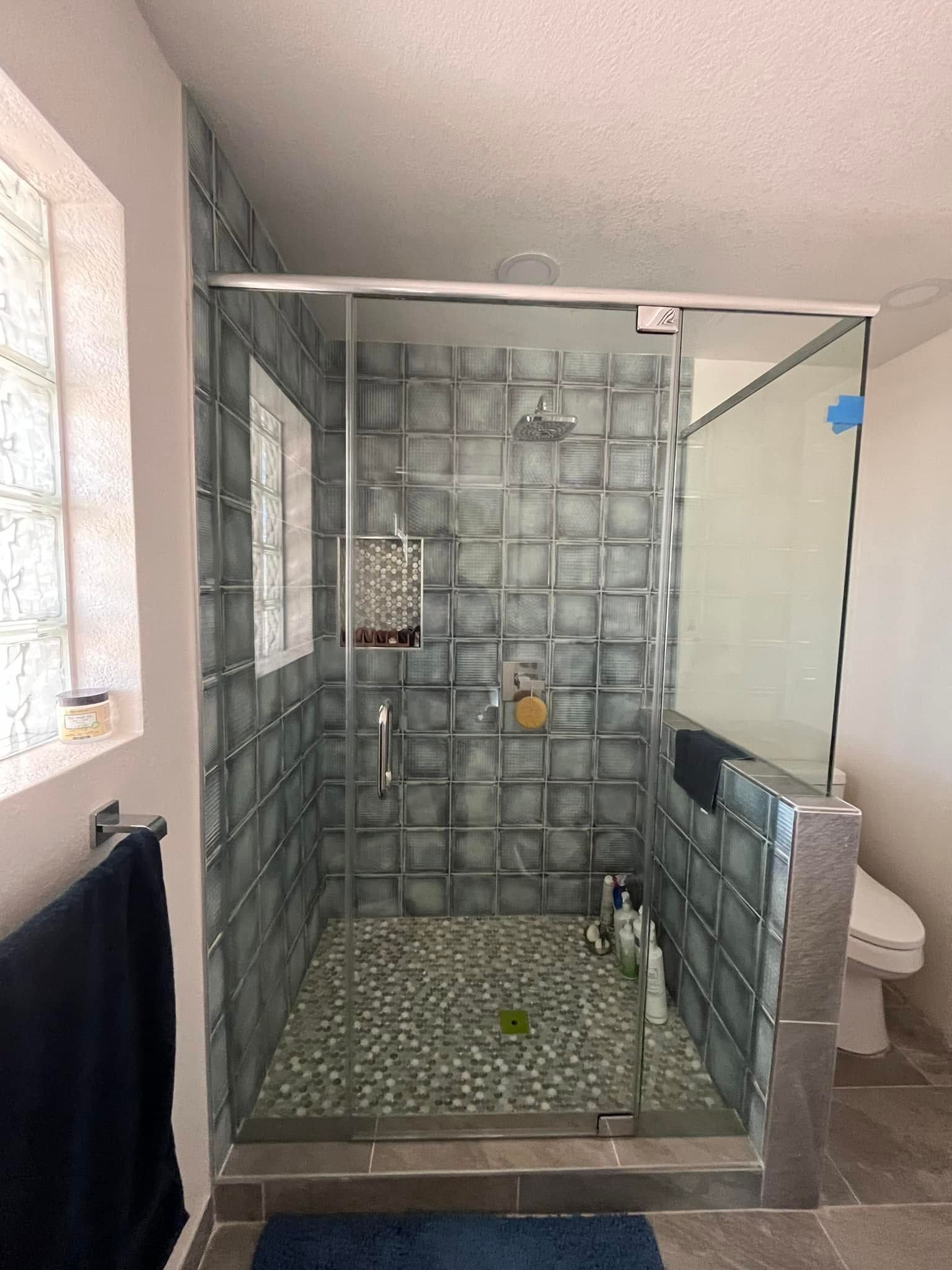 Bathroom with gray-tiled walk-in shower, pebble floor, and a glass partition beside a toilet.