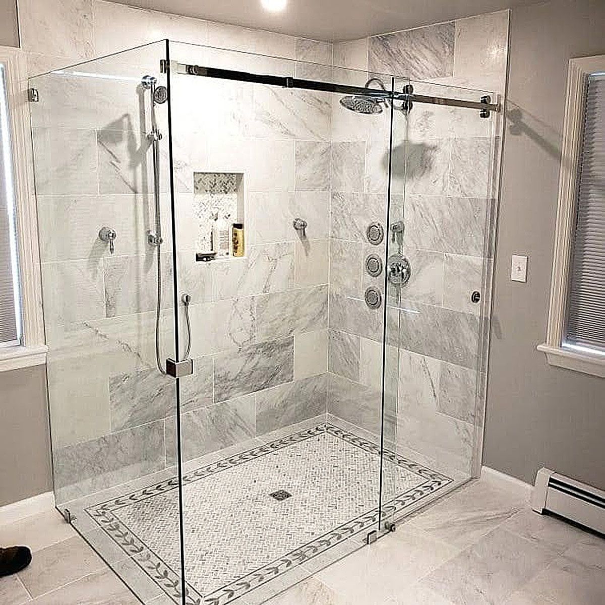 Glass walk-in shower with marble tile walls and sliding doors in a bright bathroom.