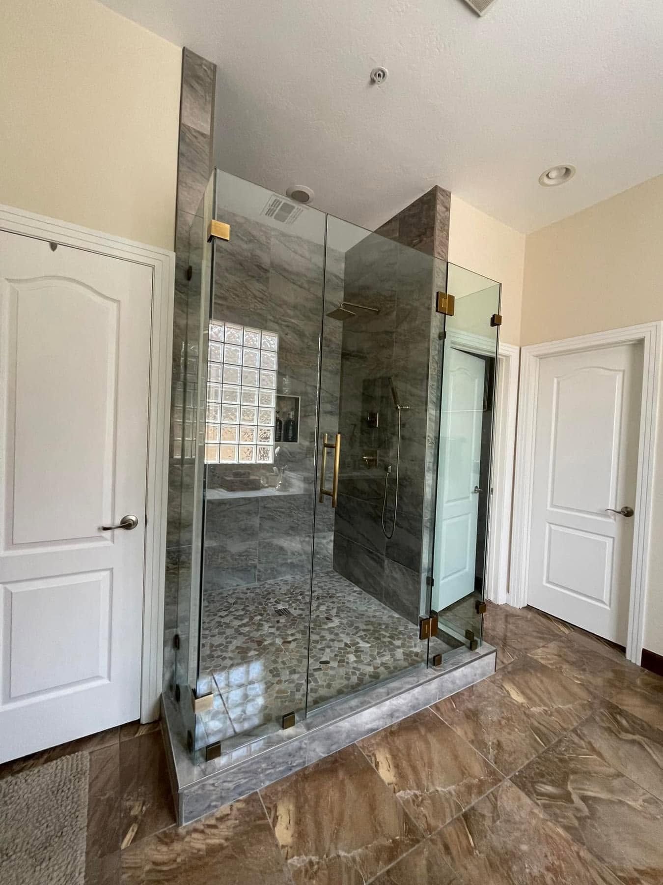 Modern bathroom with glass-enclosed shower, gray tile, and white doors on either side.