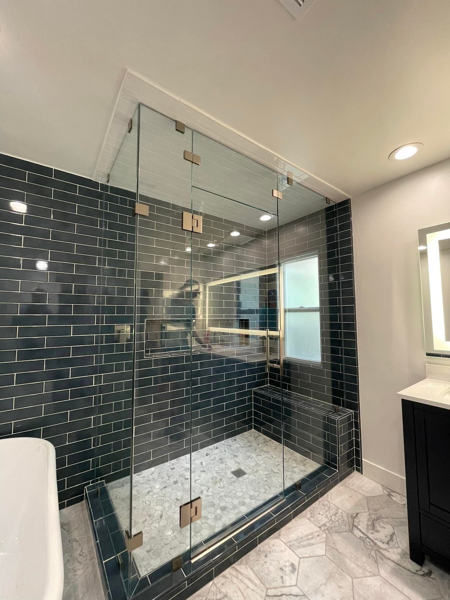 Modern bathroom with a glass-enclosed walk-in shower, black tile walls, and white hexagon floor tiles.