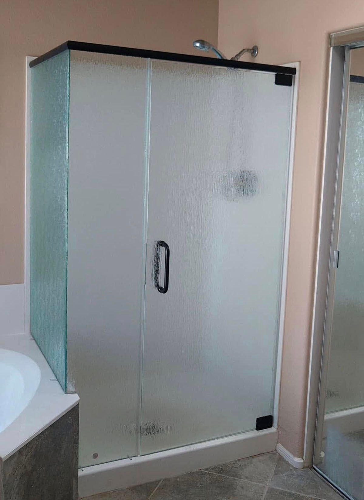 Frosted glass shower enclosure with black frame and handle in a bathroom.