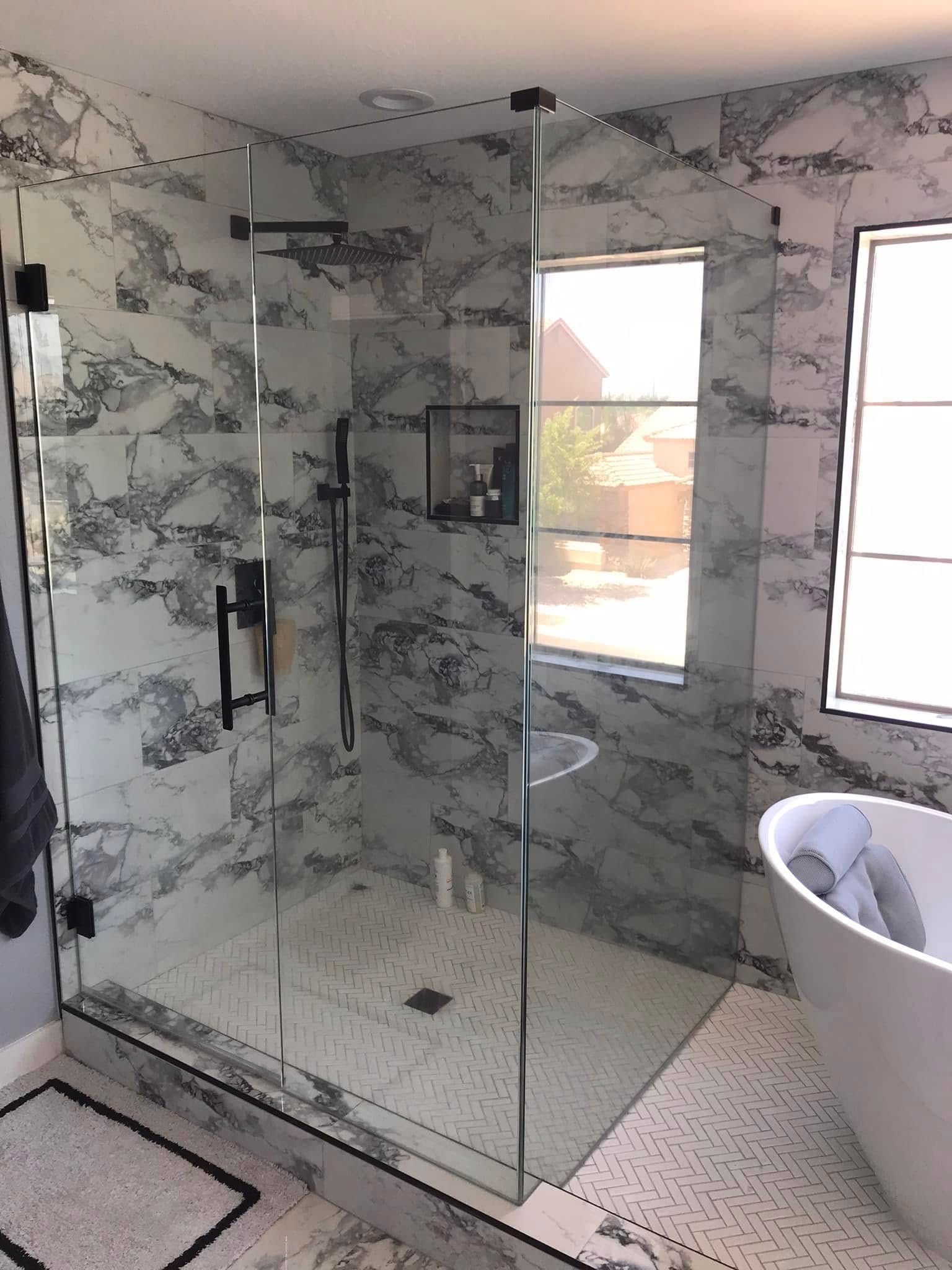 Modern bathroom with marble-pattern tile, glass shower enclosure, and freestanding tub by windows.