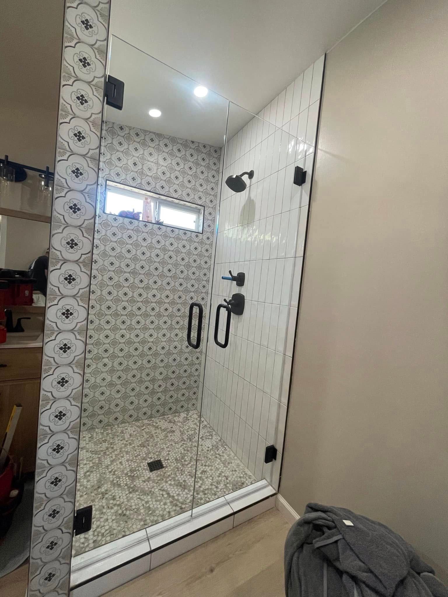 Glass shower enclosure in a tiled bathroom with black hardware and a small window above it.