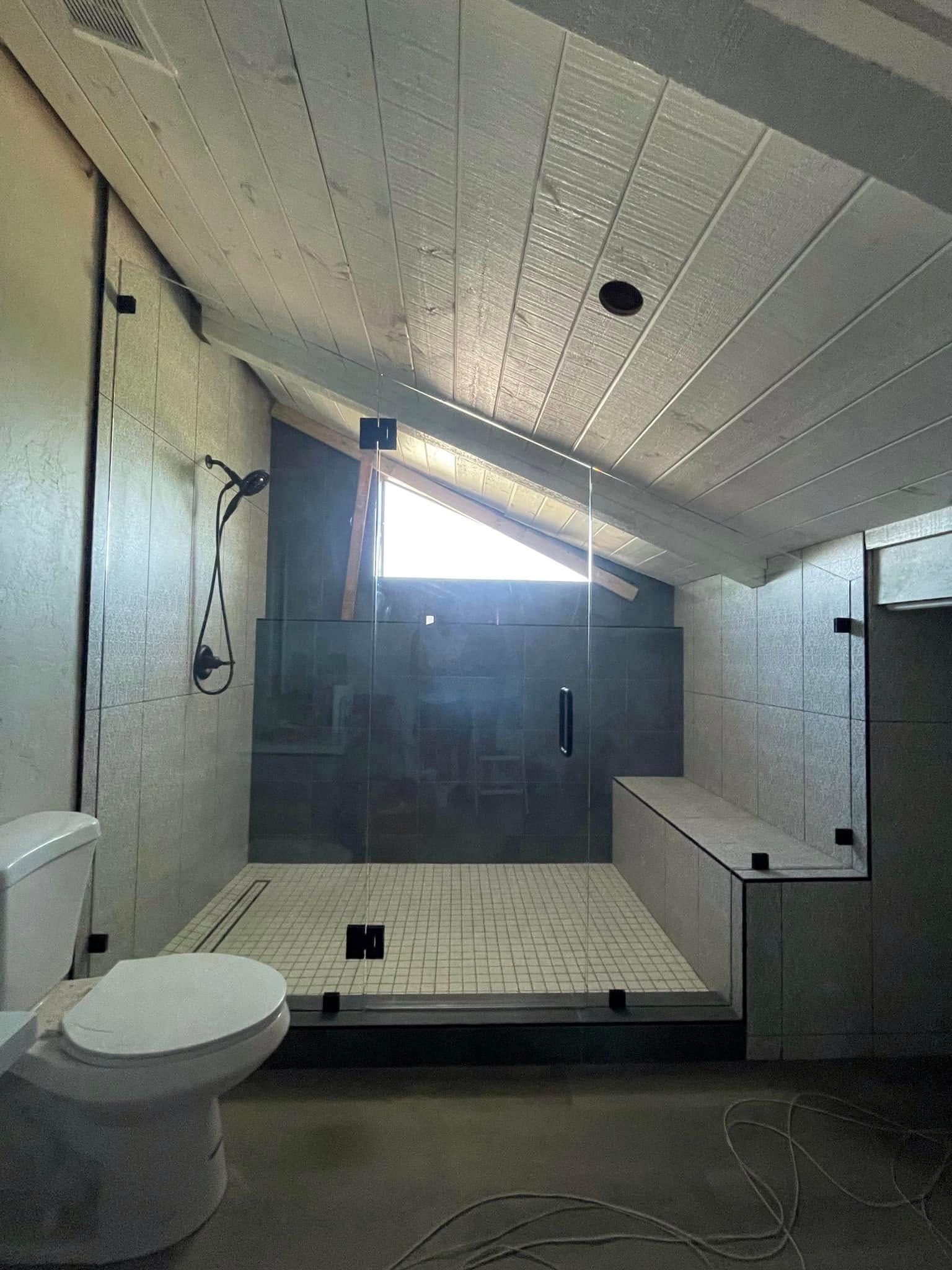Small attic bathroom with toilet, tiled shower, and slanted white ceiling with skylight.