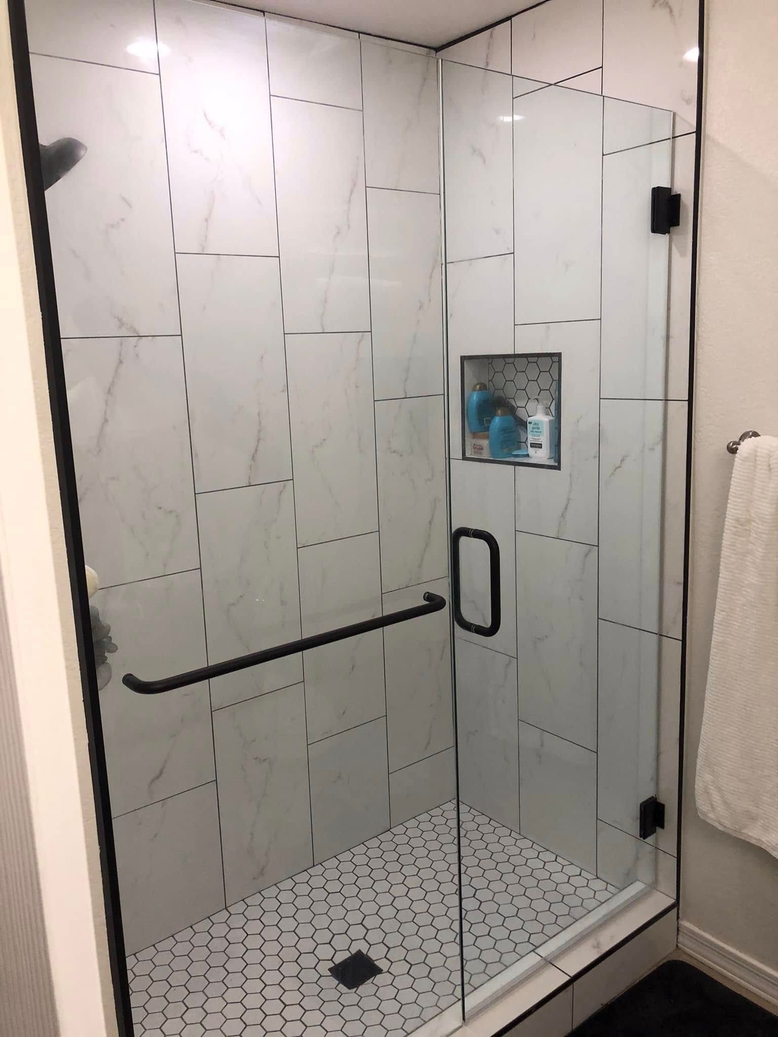 Modern glass shower stall with white tile, black grab bars, and a built-in shelf.