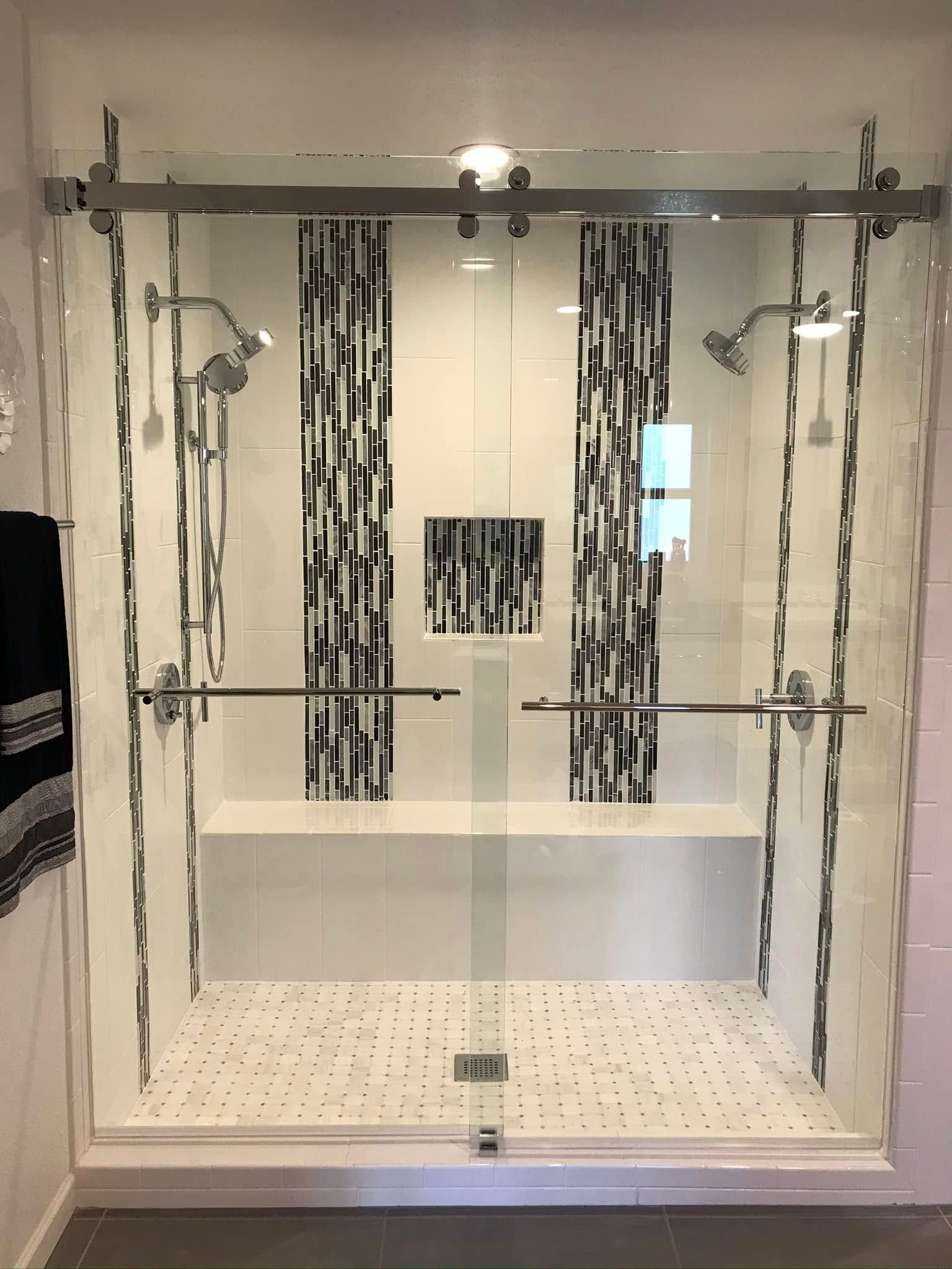 Glass shower enclosure with chrome fixtures, black-and-white tile, and a white bathtub inside.