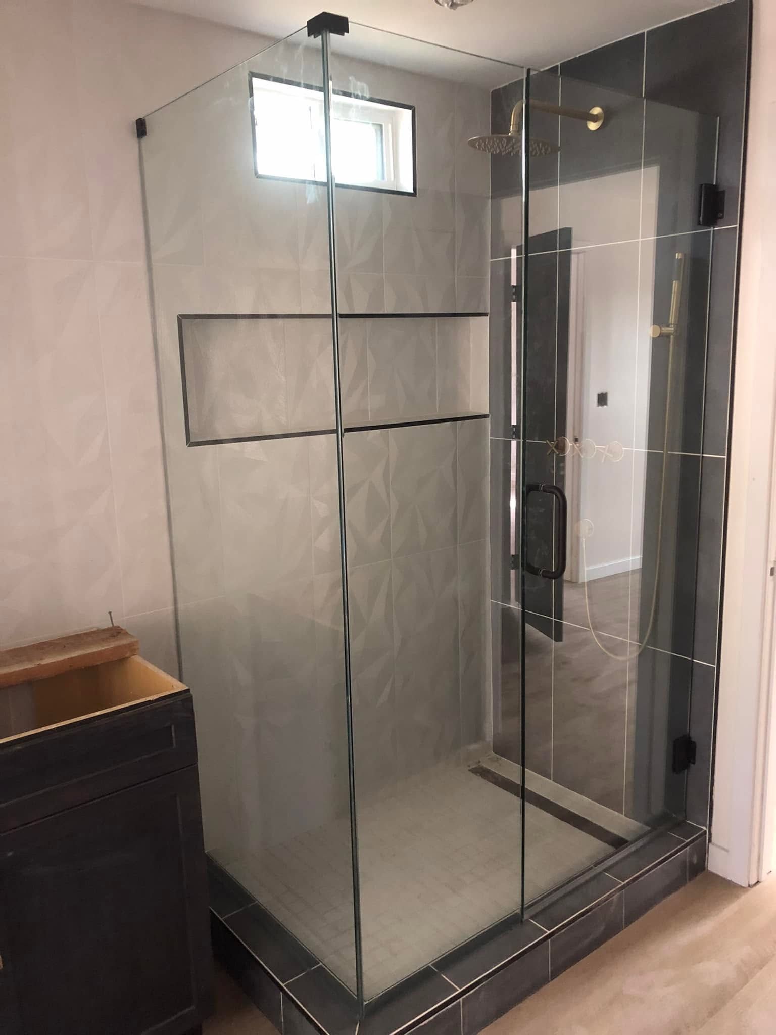 Glass shower enclosure in a bathroom with frosted panels and a small window above.