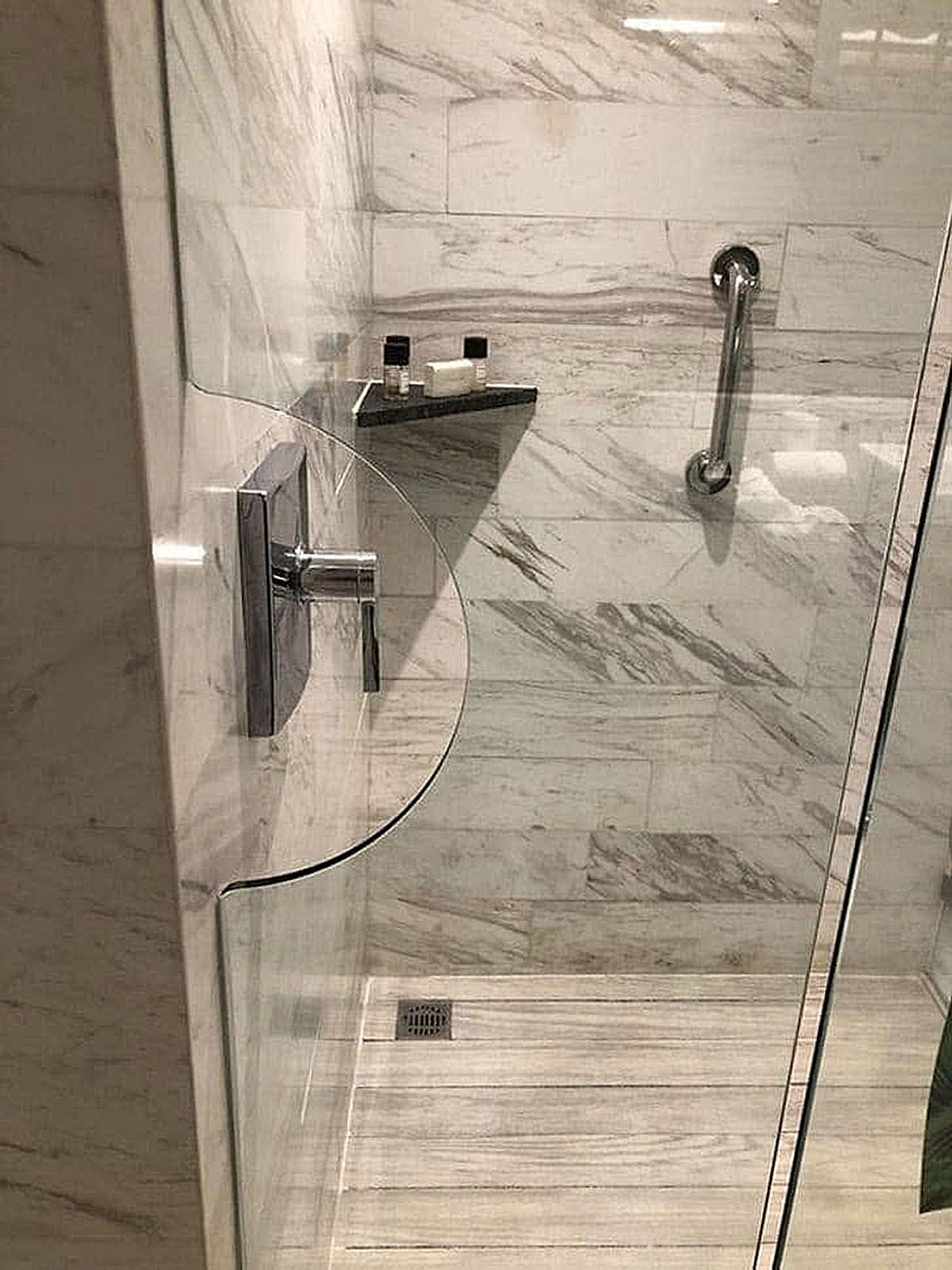 Bathroom shower with glass door, marble tile walls, and a built-in shelf.