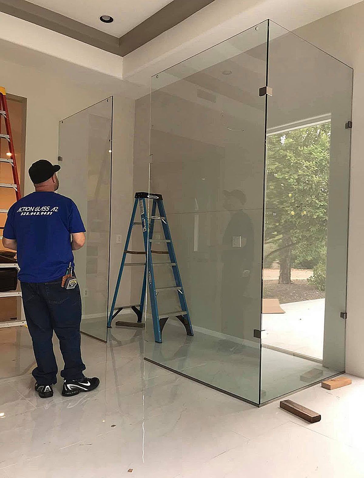 Worker installing a large glass partition inside a bright room, with a ladder nearby.