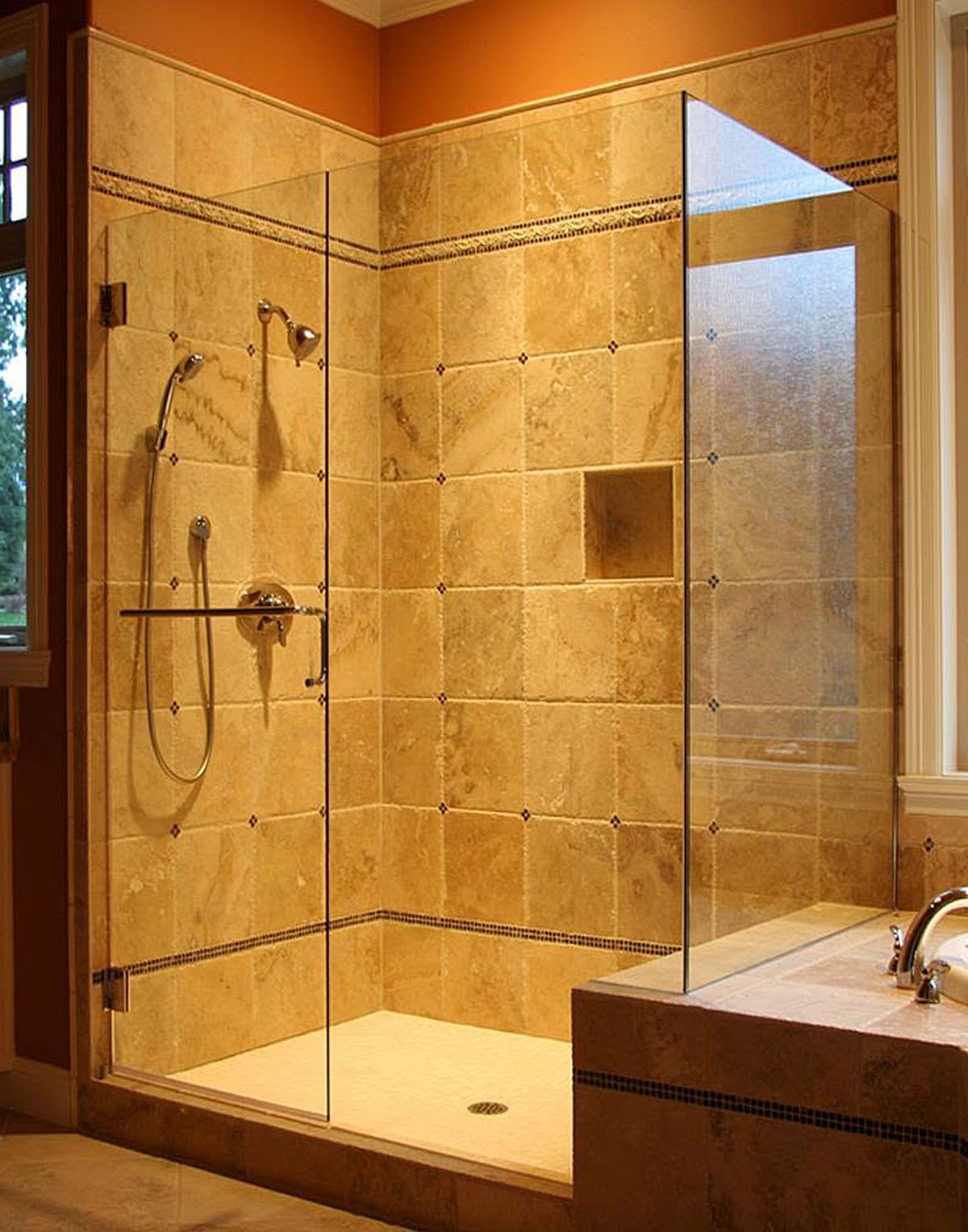Glass-walled beige tiled shower with built-in niche and chrome fixtures in a bathroom.