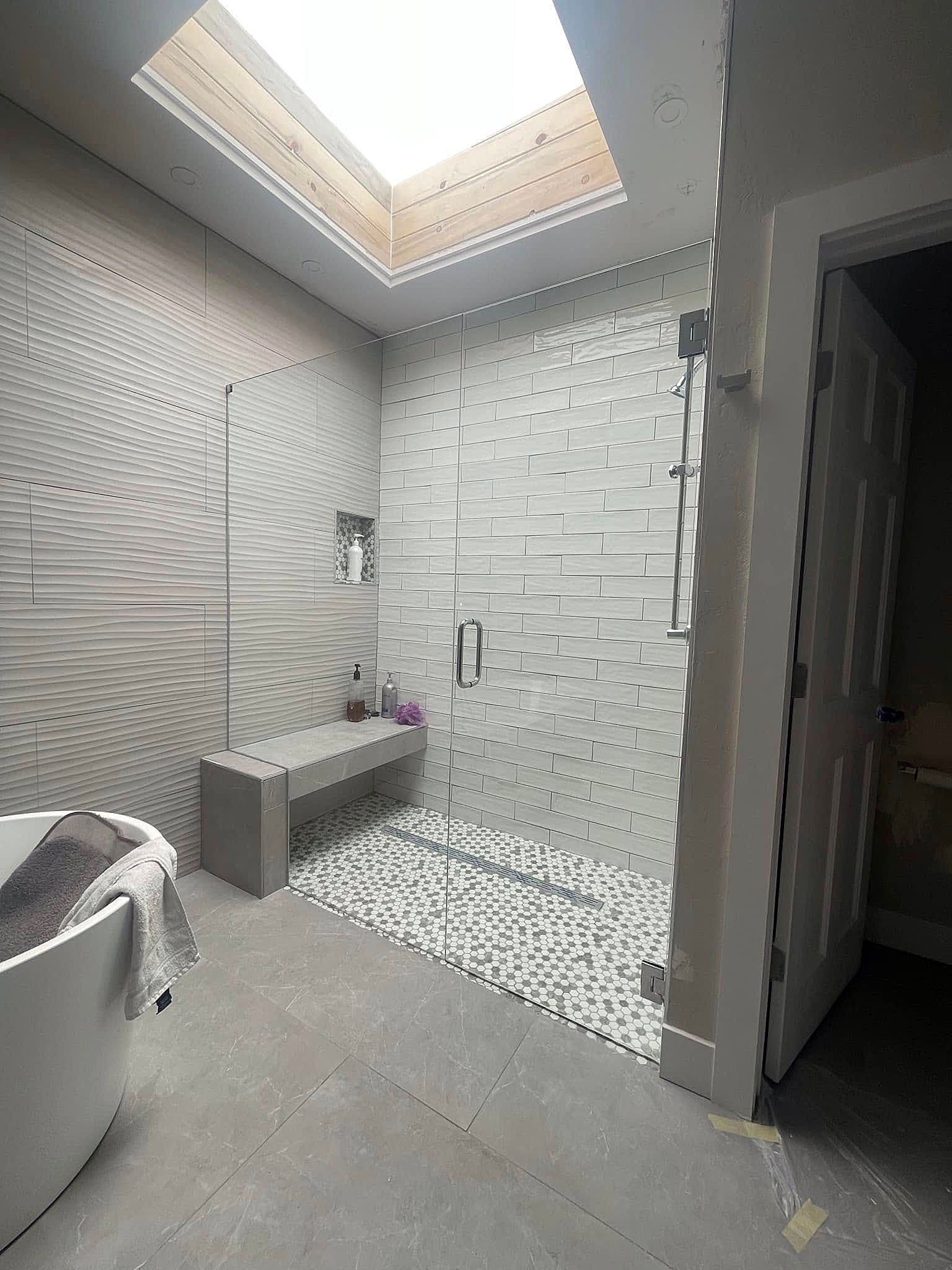Modern tiled bathroom with walk-in shower, skylight, and bench seat.