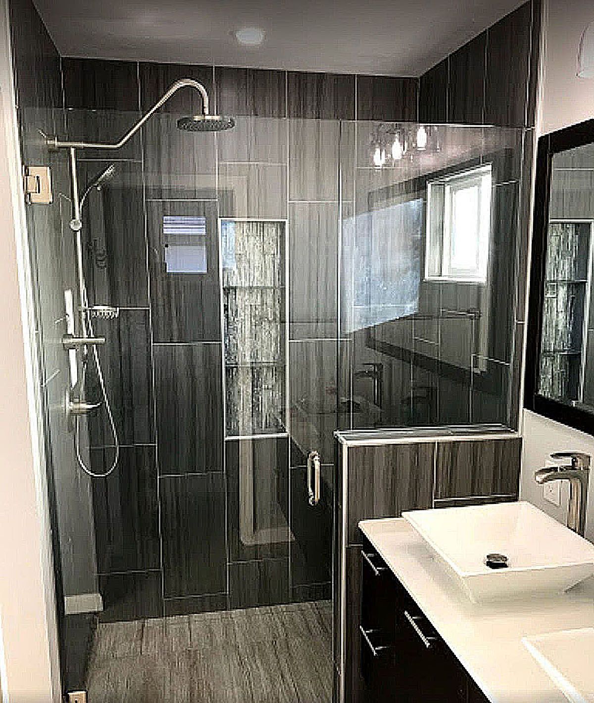 Modern bathroom with glass shower, dark tile, and white sink vanity.