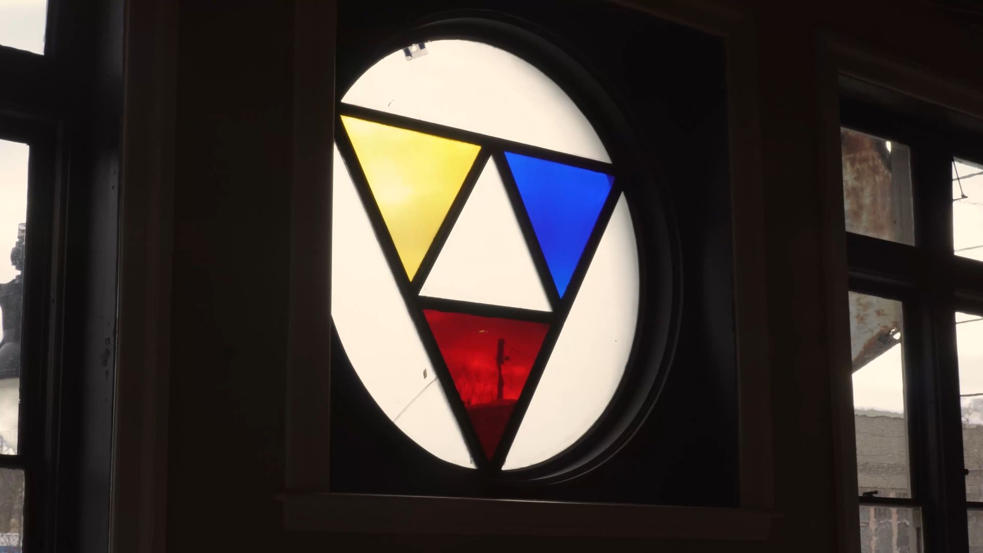 Abstract stained-glass window with yellow, blue, red, and white geometric shapes in a dark frame.