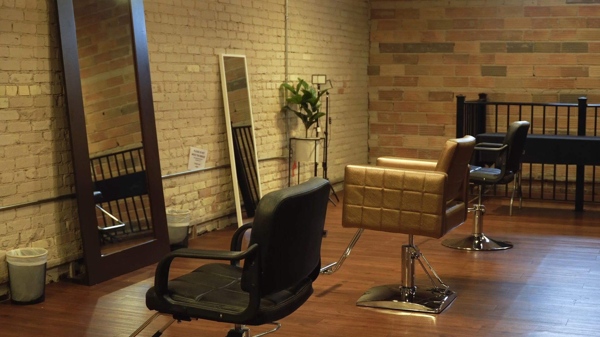 Modern salon interior with styling chairs, mirrors, brick walls, and wooden floors.