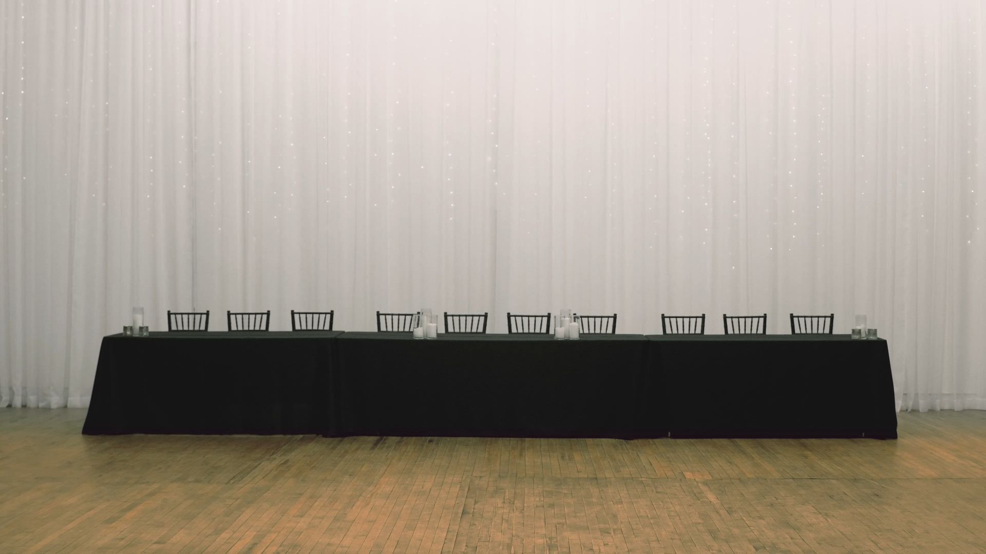 Long black table with small signs or labels on a wooden floor in front of a white curtain backdrop.