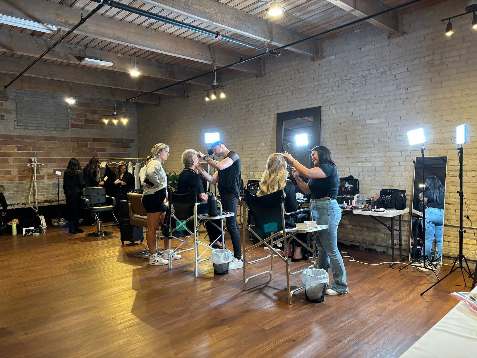 Salon workspace with stylists and clients under bright lights in a brick-walled room
