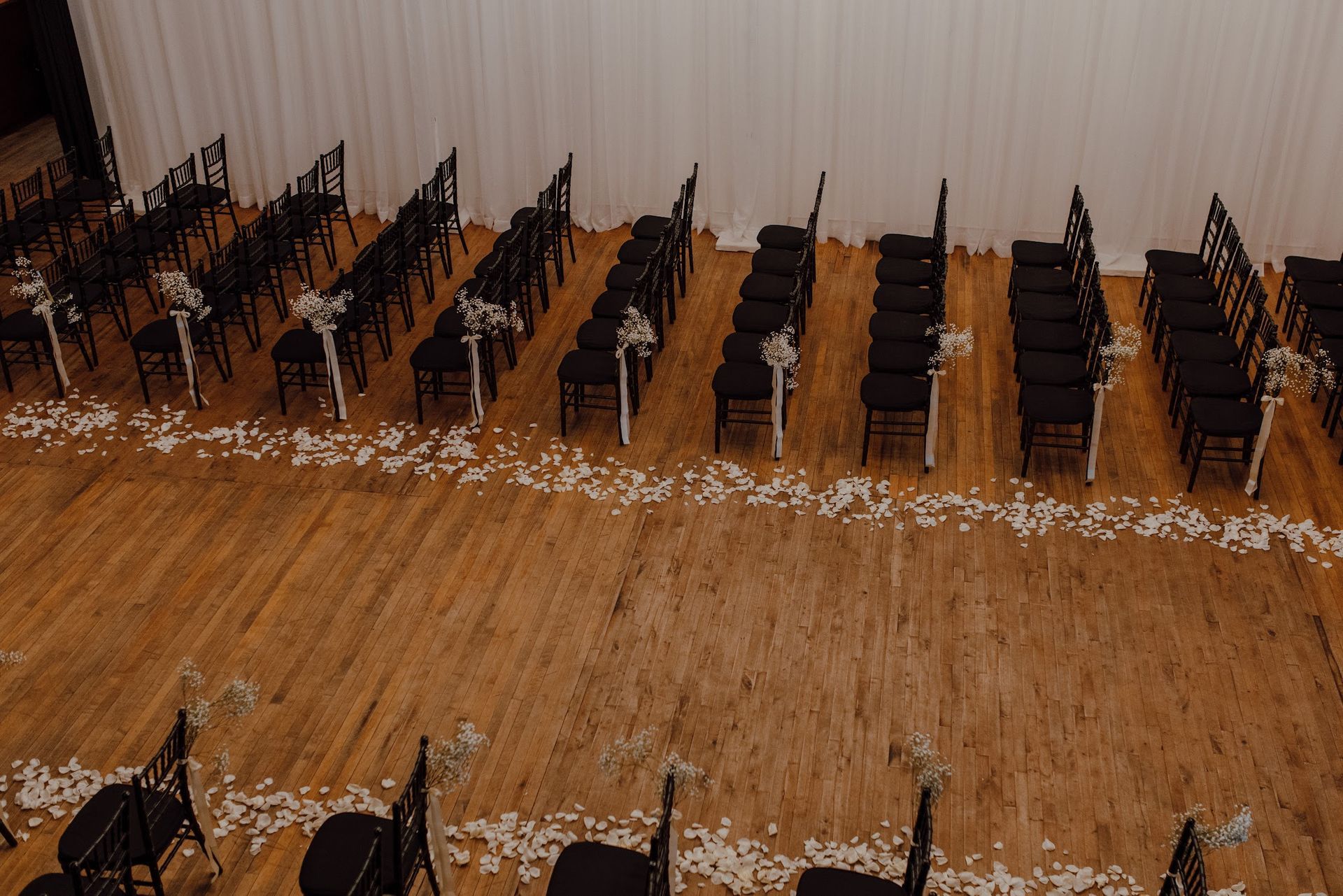 Empty auditorium with rows of black chairs on a wooden floor near a plain wall.