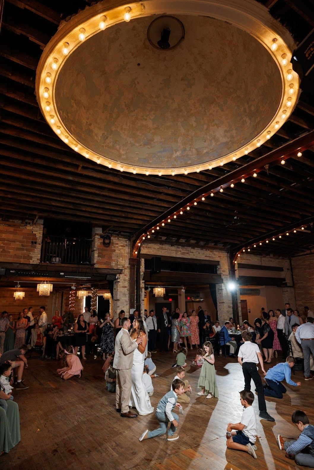 People dancing in a large hall beneath a glowing circular ceiling light.