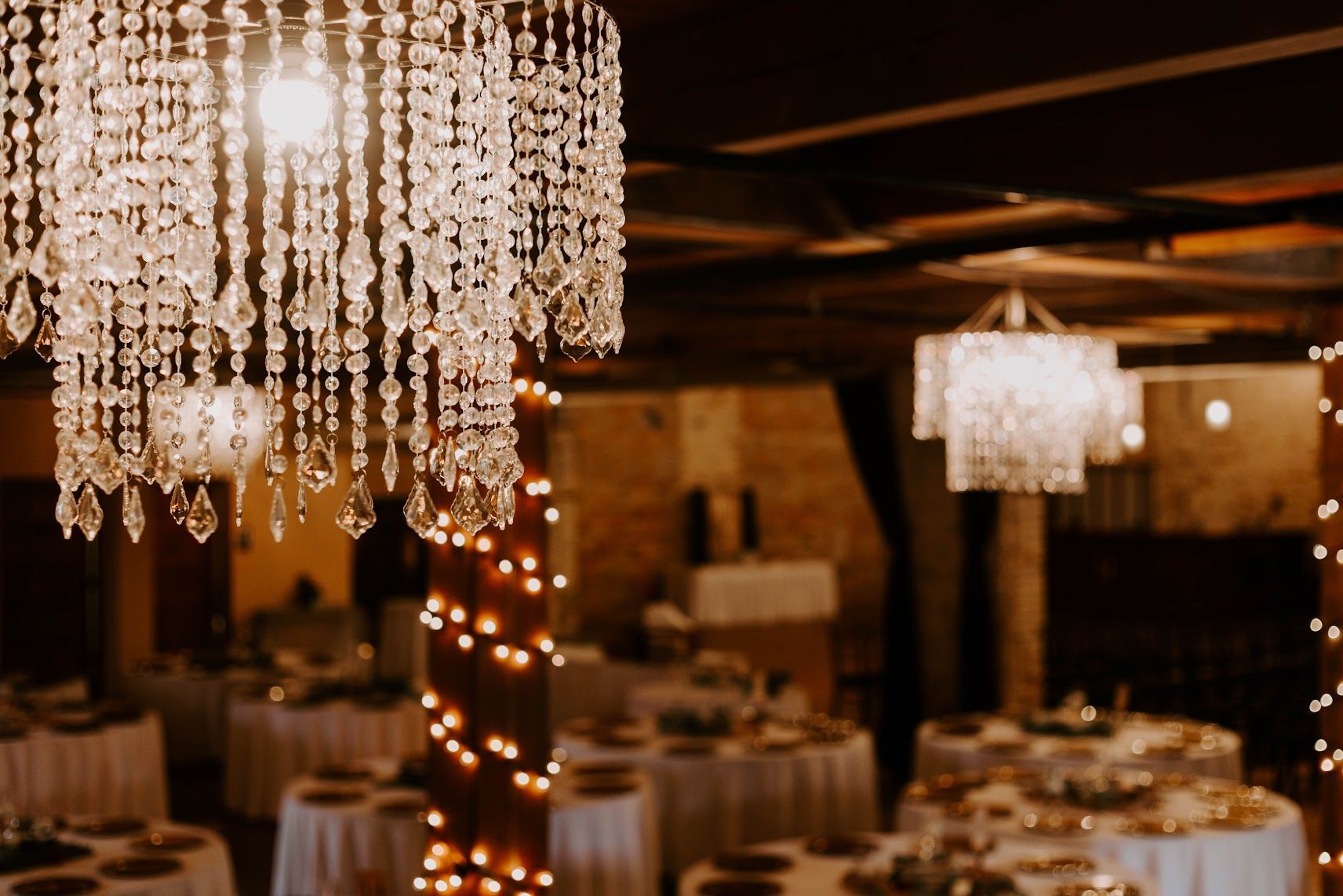 Elegant banquet hall with crystal chandeliers, warm string lights, and set dining tables at night