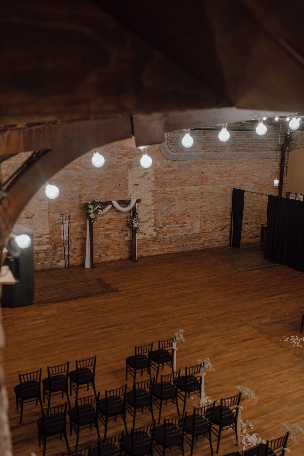 Empty rustic event hall with wooden floor, brick wall, and hanging string lights