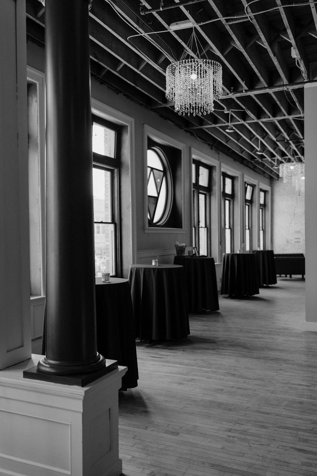 Elegant black-and-white hall with tall windows, chandeliers, and cocktail tables along a polished floor