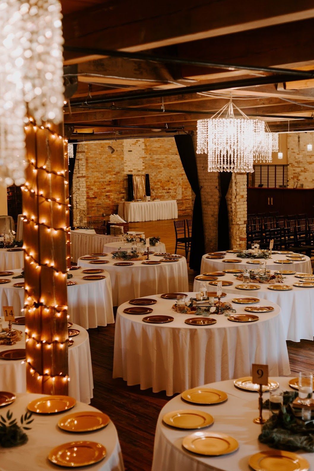 Elegant banquet hall with round white-clothed tables, gold accents, and warm string lights