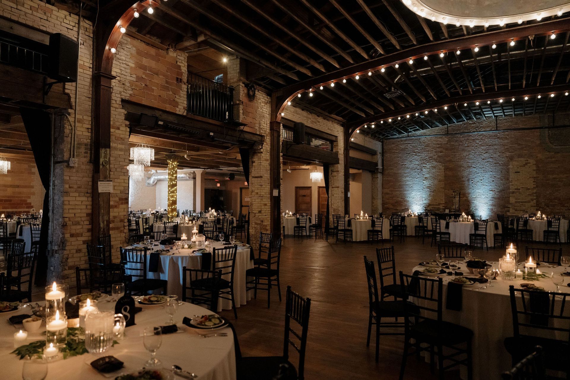 Elegant brick banquet hall with round candlelit tables and arched wooden ceiling beams