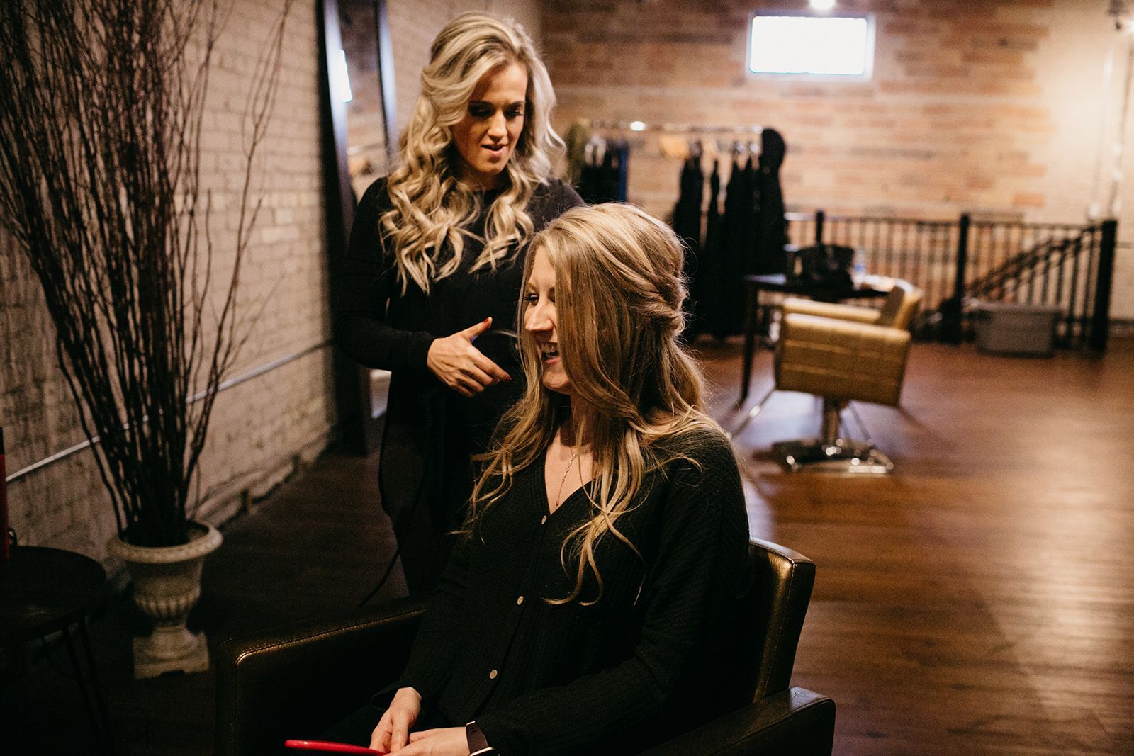 Stylist working on a woman’s hair in a salon with warm lighting and wooden floors