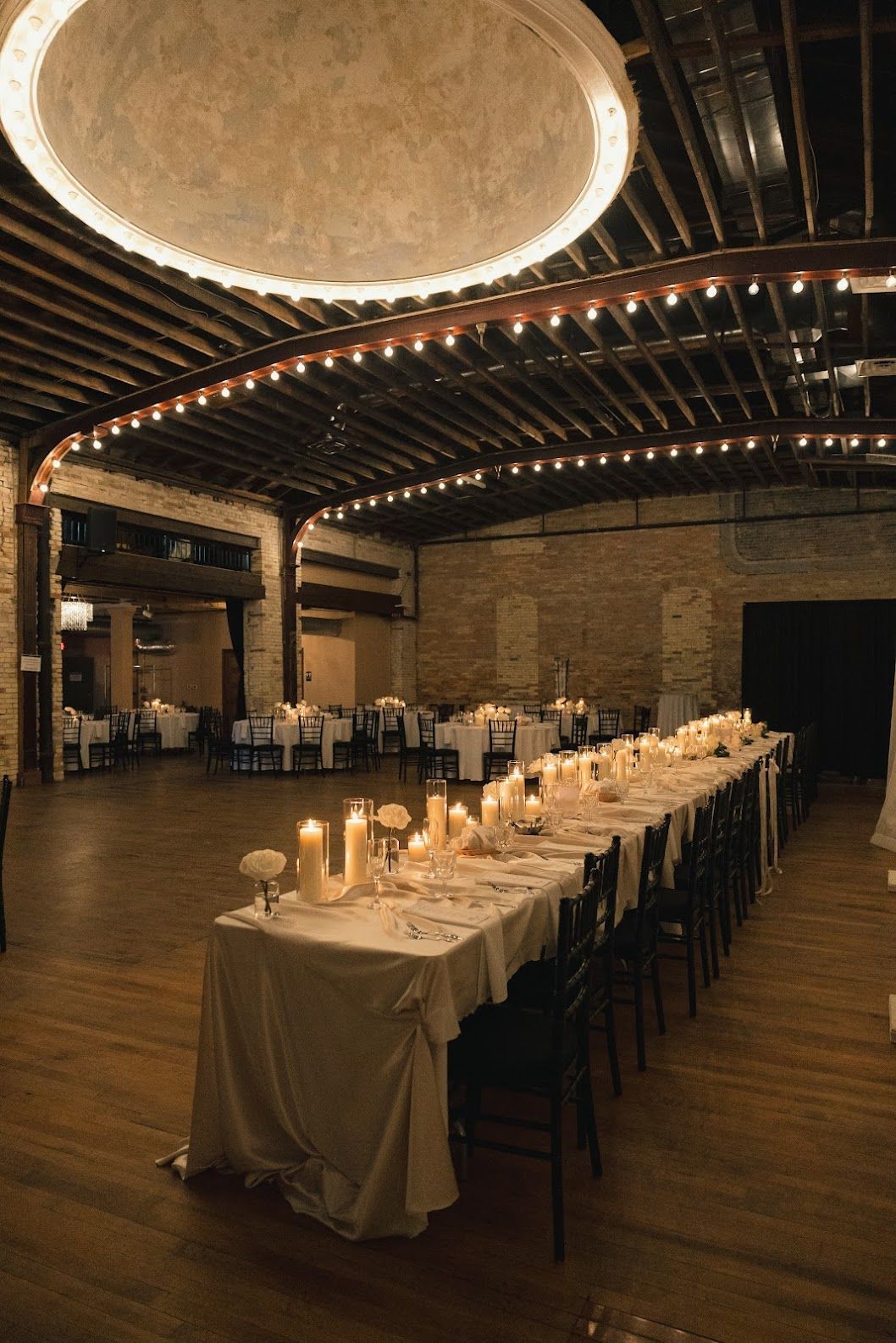 Long candlelit banquet table in a rustic hall with arched brick ceiling and wooden floor