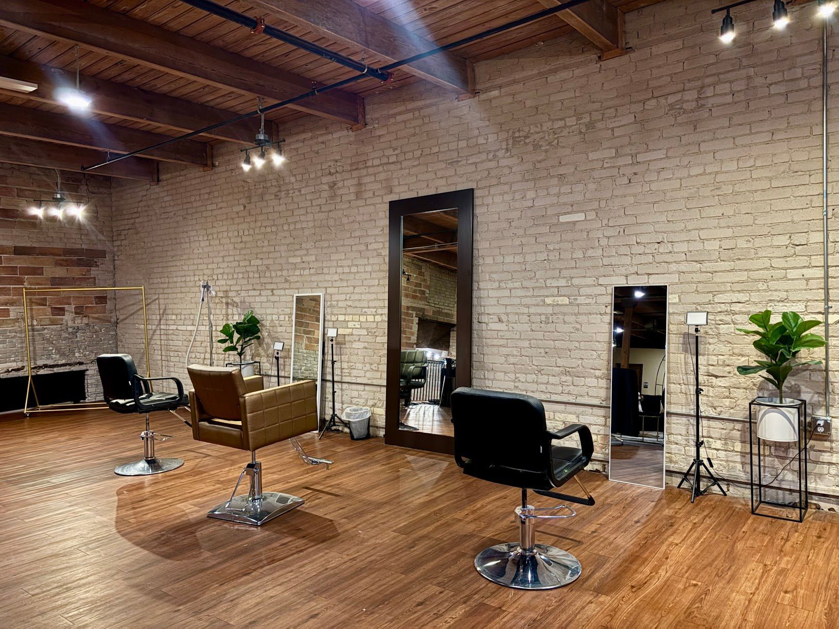 Empty modern hair salon with styling chairs, mirrors, wood floors, brick walls, and potted plants