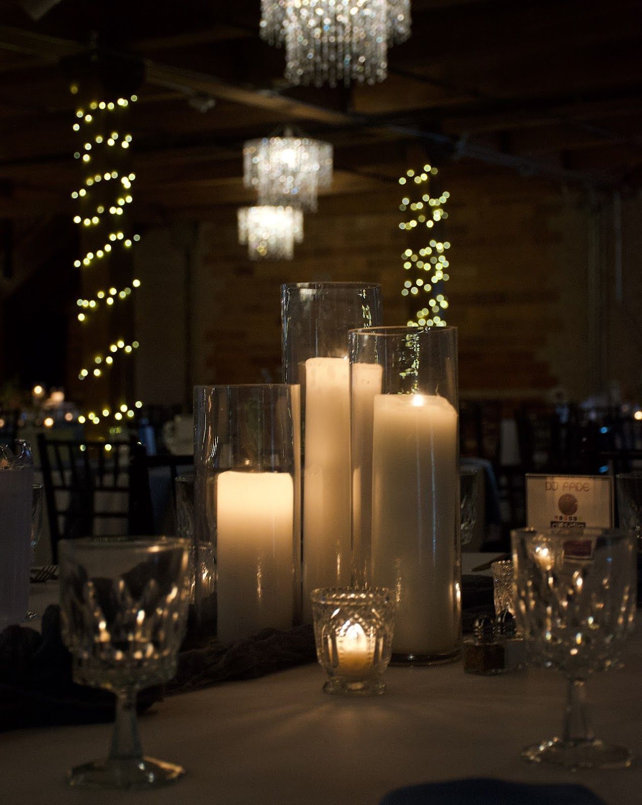 Candlelit dinner table with glass vases, lit candles, and soft holiday lights in a dim banquet room