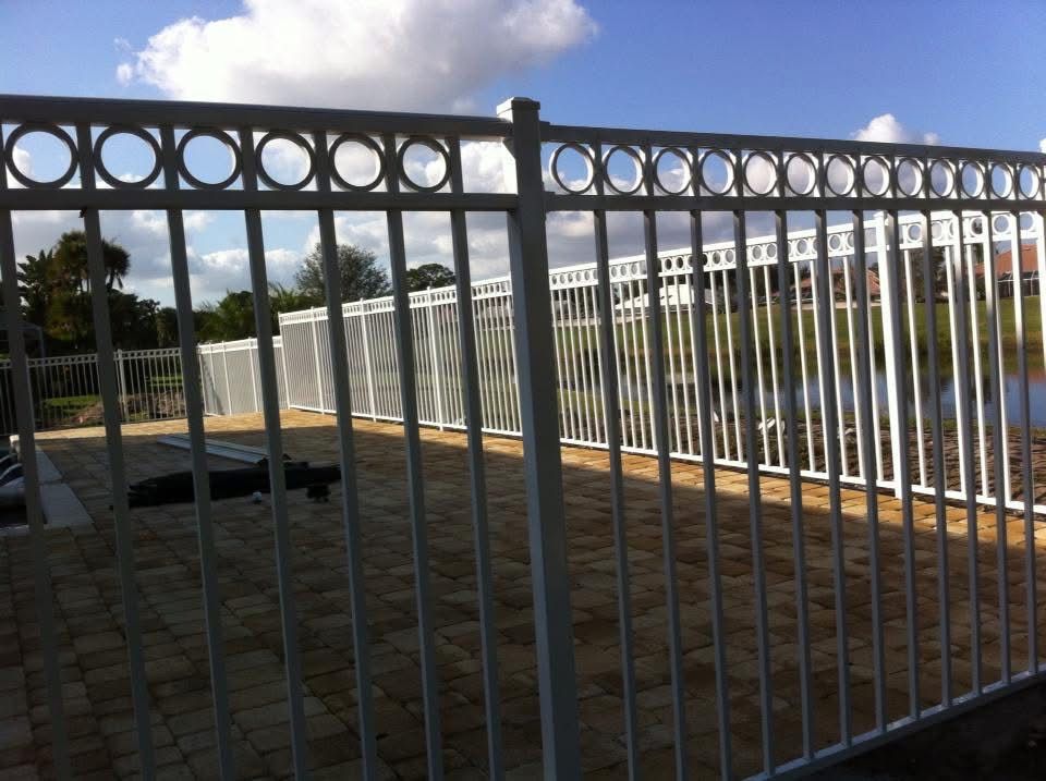 A white metal fence surrounds a brick walkway overlooking a body of water