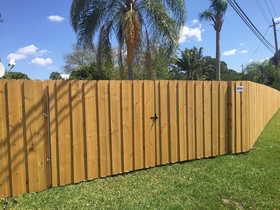 A wooden fence with a gate and palm trees in the background.