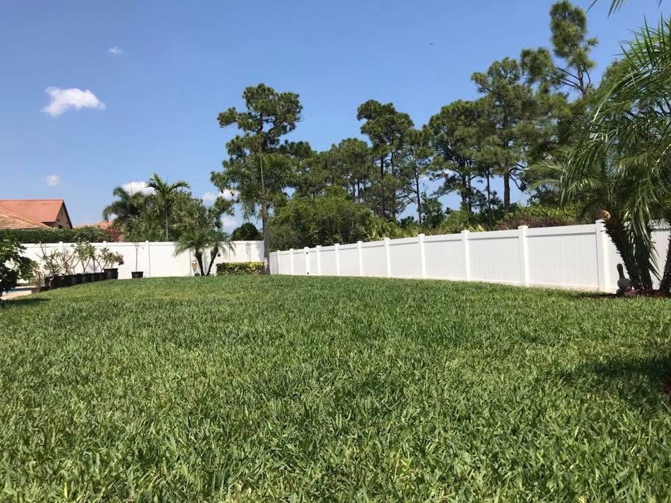 A large lawn with a white fence and trees in the background.