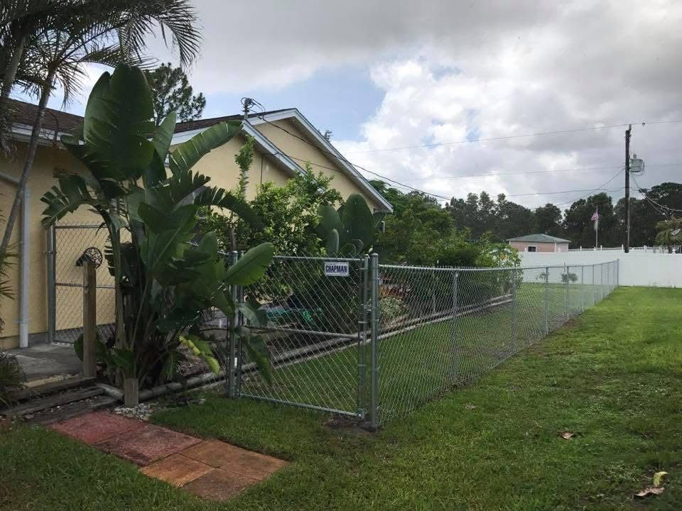A chain link fence surrounds a lush green yard in front of a house.